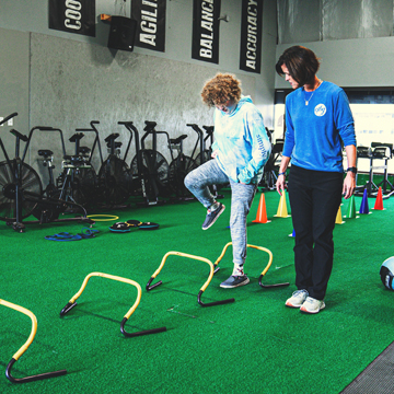 Athlete performing hurdle steps while being watched by a coach.