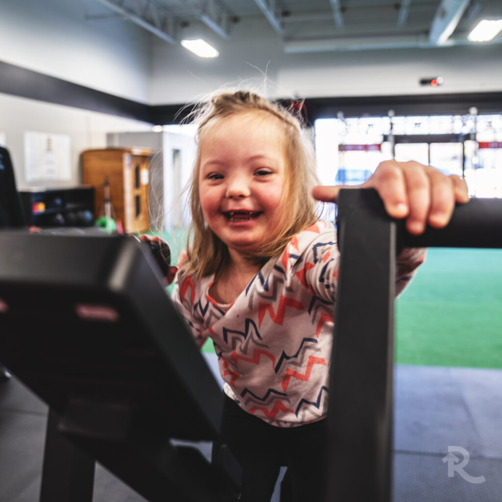 A young female athlete with Down syndrome smiles while using the Rogue Echo Bike