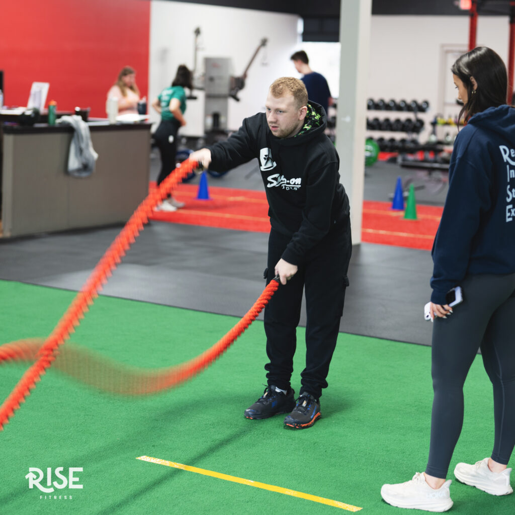 A young male athlete uses the battle ropes while a coach watches the movements.