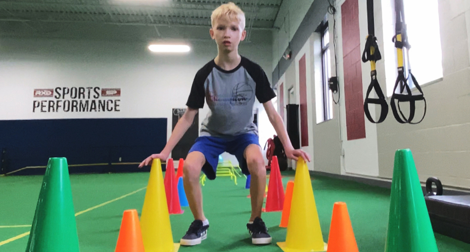 Young athlete squatting and touching brightly colored cones.