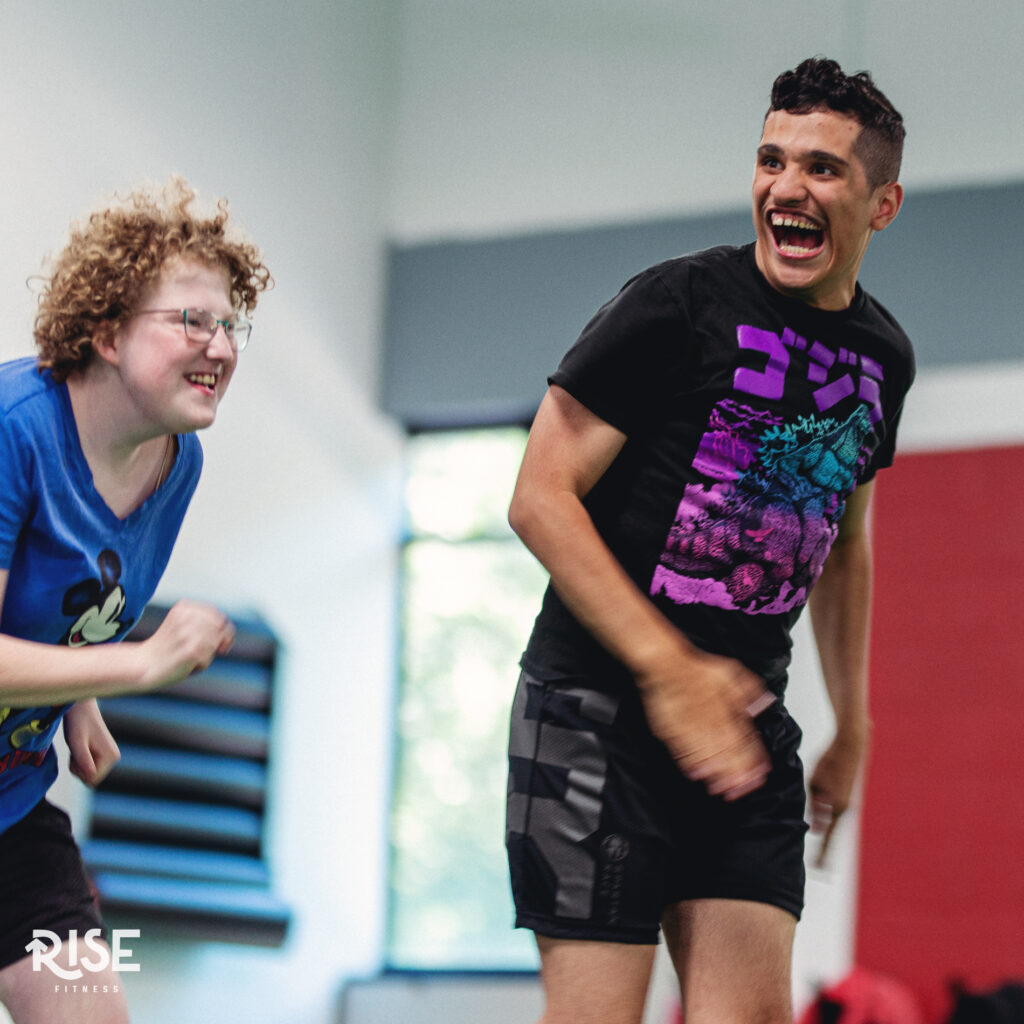 A young male and young female athlete with big smiles on their face as they are about to begin racing each other in the gym.