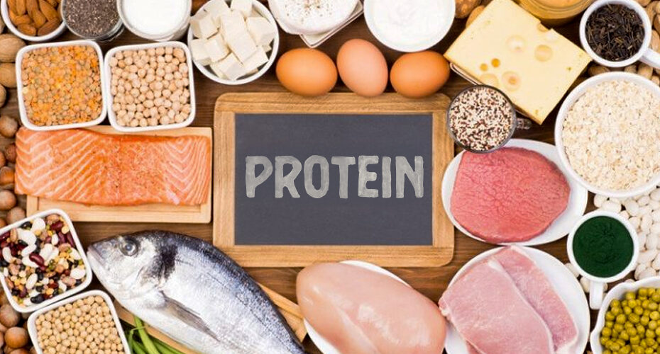 A vareity of natural protein sources all spread out evenly on a wood table top. There is a small chalkboard in the center with the word "protein" written on it.
