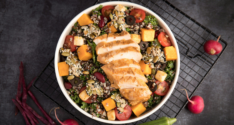 A top down view of a food bowl on a table. The bowl is filled with healthy and colorful foods.